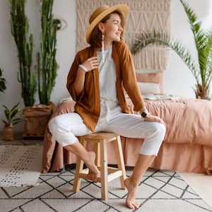 A fashionable young woman sitting on a wooden stool in front of her bed with a macrame headboard