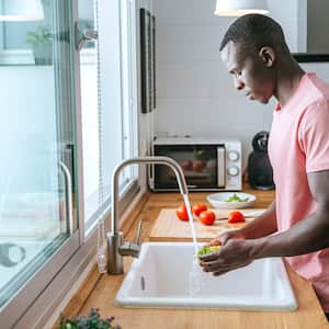 A young man washing vegetables in a kitchen sink