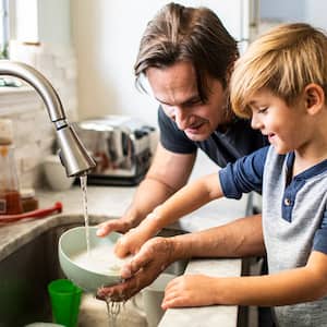 Father and son wash dishes in the kitchen sink