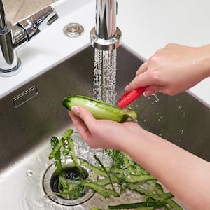 A woman peeling a cucumber over a garbage disposal