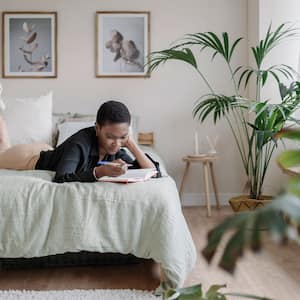 A woman writing in her notebook while laying on her comfortable bed