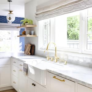 a home kitchen with white cabinets, marble countertop, gold fixtures, blue walls, and light streaming through the window
