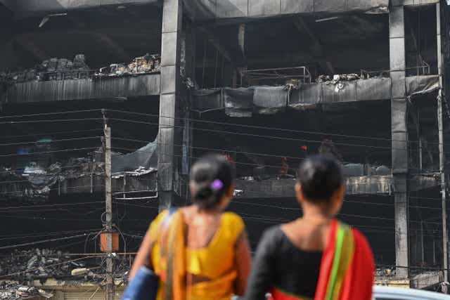 <p>Onlookers gather outside a burn down commercial building a day after a fire broke out, in New Delhi</p>