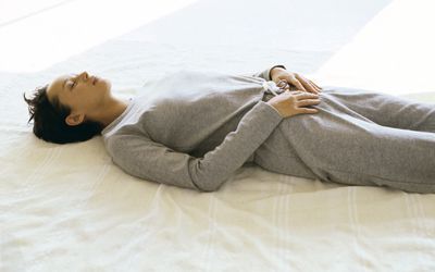 Woman wearing athletic wear lying on back with hands placed on lower abdomen