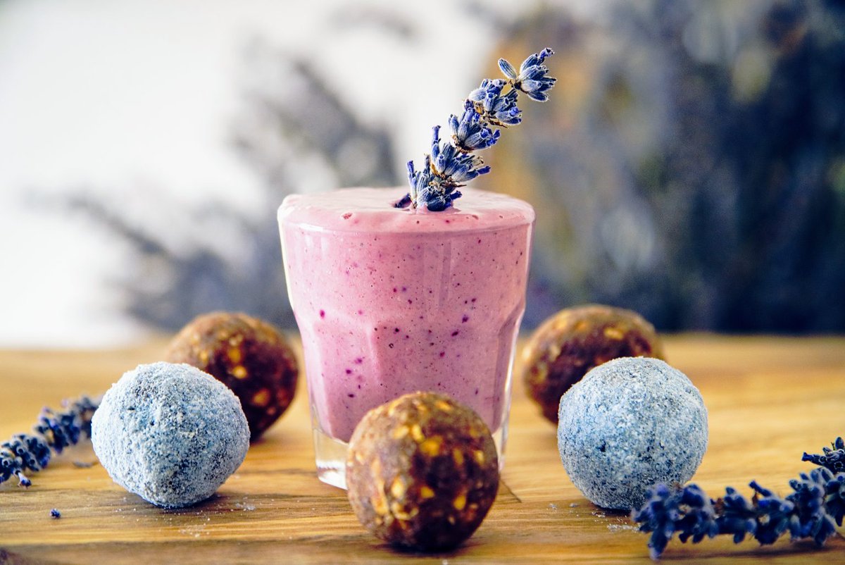 Glass of a pink smoothie on a wooden table decorated with purple plants.