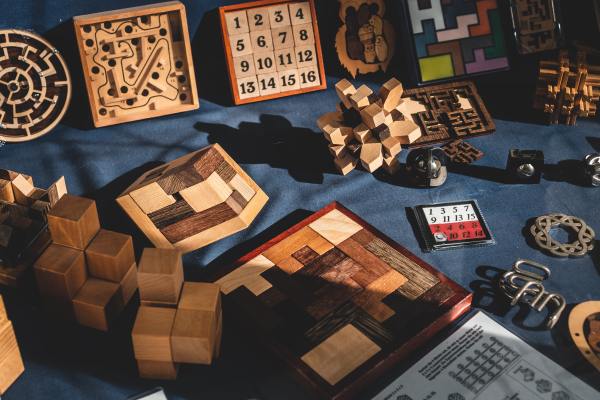 Many puzzles made of different colored woods, metal, and paper, all on a dark blue cloth.