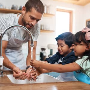 Father and children washing hands in kitchen sink