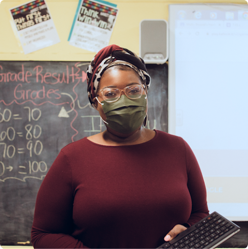 Teacher standing in front of a blackboard holding a keyboard.