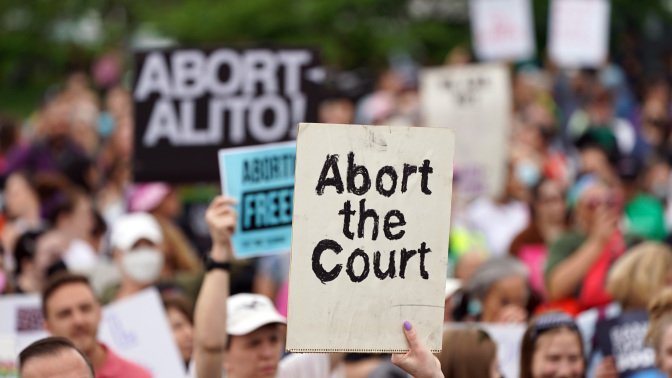 A sign being held above a crowd that reads "Abort the court."