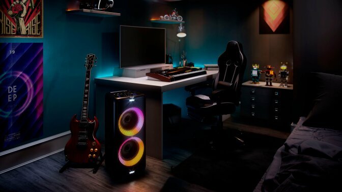 Black speaker with pink and yellow lights in bedroom with guitar, computer, and toys