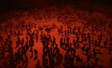 A large horde of zombies is lit by a menacing red light.