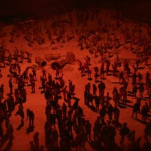 A large horde of zombies is lit by a menacing red light.