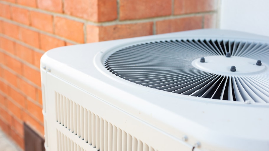 Close-up of an HVAC system in the backyard of a red brick house