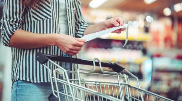 Woman stands next to grocery cart looking at receipt