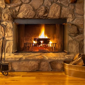 a stone fireplace with wood and fire with a bucket of firewood to the right