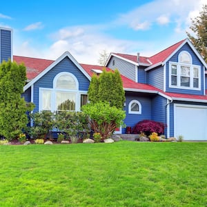 view of bright blue suburban home with green yard and landscaping