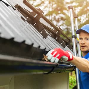 A worker cleans a house’s gutter from leaves and dirt