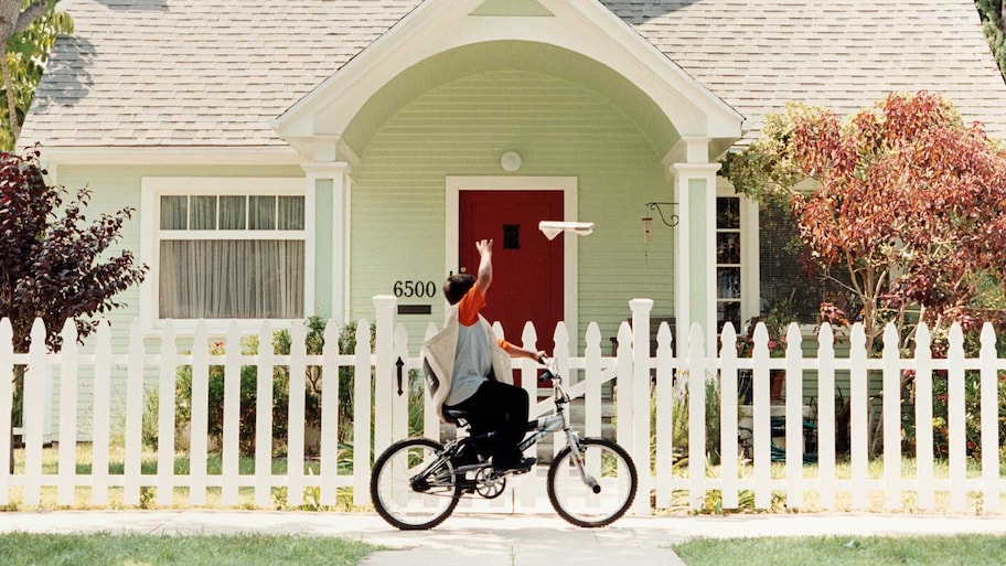 Paperboy throwing newspaper in a house with white fence