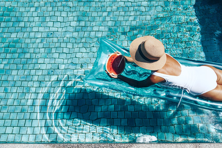 Menina que flutua na praia colchão e comendo melancia na piscina azul. dieta da fruta tropical. Férias de verão idílico. Vista de cima.