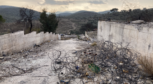 A concrete wall defining a border, where stacks of barbed wire can be seen.