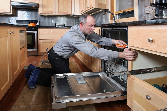 Worker installing energy efficient dishwasher in beautiful kitchen.