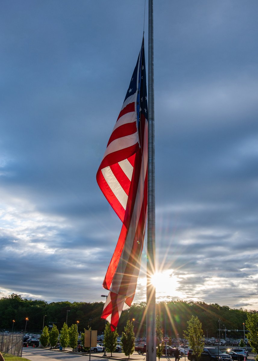 The sun rises over the trees in the background with the flag in front.
