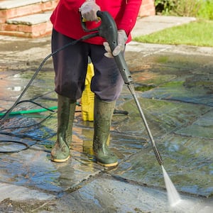 A person pressure washing a patio of a house