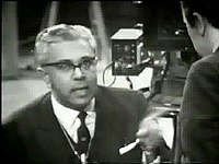 Screenshot of a bespectacled Savundra, with David Frost's back to the camera