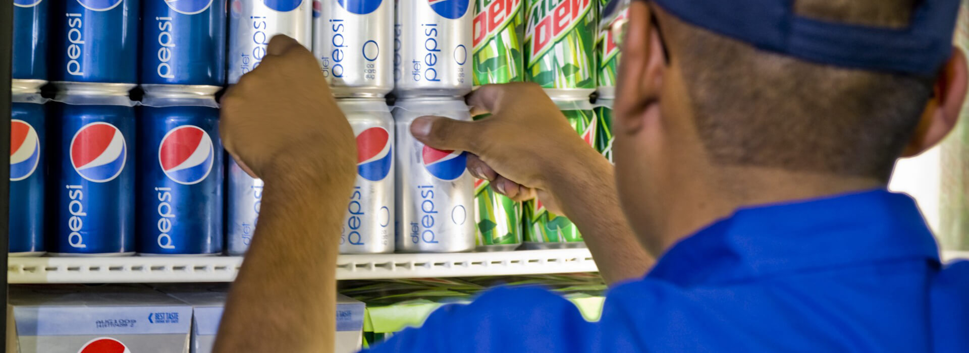 Worker loading cans of Pepsi into a refrigerator.