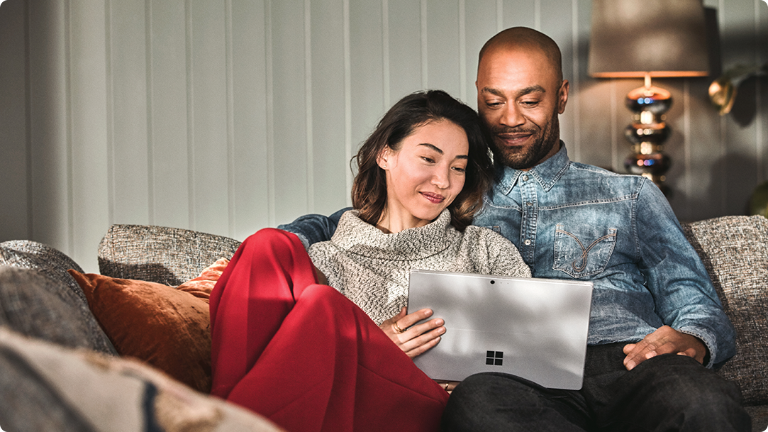 Man and woman sitting on a couch looking at their laptop