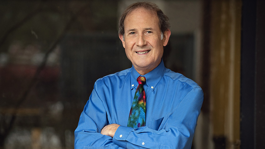 man smiling in rainbow tie in blue shirt