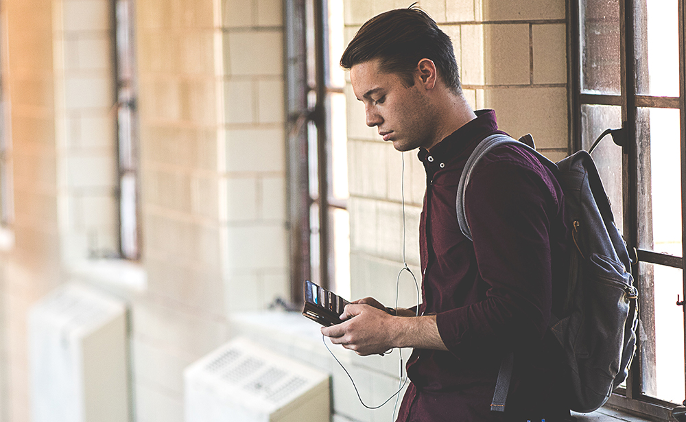 Student with backpack and earphone on looking at his cellphone