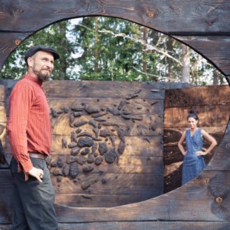 A man and a woman stand among wooden panels and sculptures in a park.