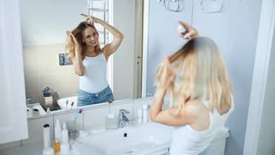 Woman in the bathroom using hairspray in front of the mirror