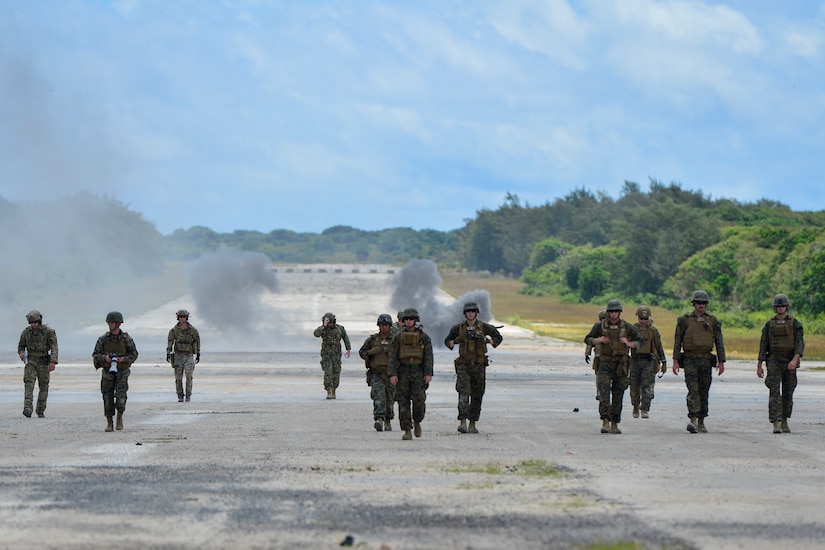 Marines and sailors walk on an airfield.
