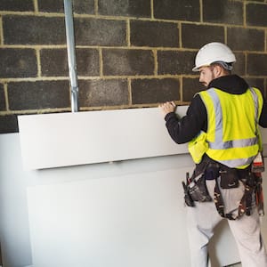 Worker picking up sheet of drywall