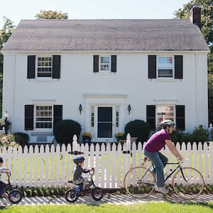 Father and kids riding bikes in front of fenced house