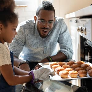 A father and her daughter baking muffins in the oven