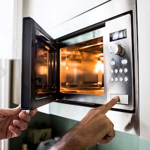 A man’s hand reheating food in the microwave