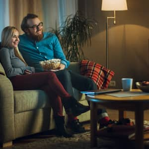 A couple sits on a couch in a warmly lit living room 