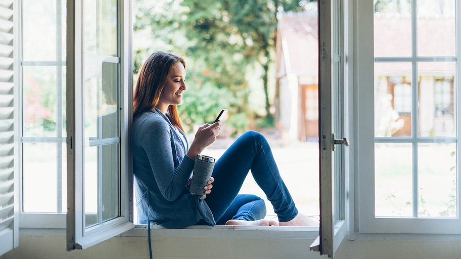 woman looking at phone near open window