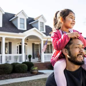 Daughter on father's shoulders in front of suburban home