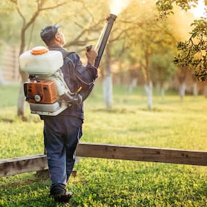 A worker using a sprayer for mosquitoes in a yard