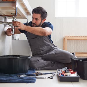 Plumber is fixing a leaking sink in the bathroom