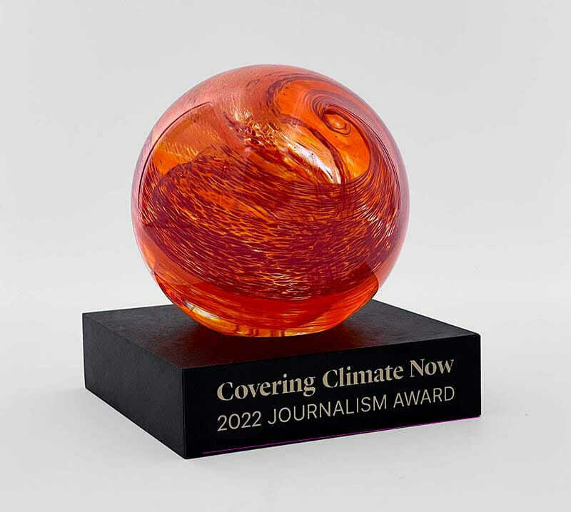 An image of a red, glass-looking ball on a black base. The base has the words "Covering Climate Now 2022 Journalism Award" on the front.