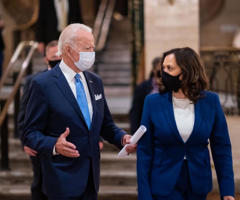 President Biden and Vice President Harris speak to each other while wearing masks and blue suits