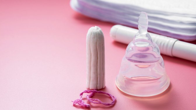 An upside down menstrual cup sits next to a tampon on a pink table.
