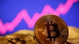 FILE - A representation of virtual currency bitcoin is seen in front of a stock graph in this photo illustration created Jan. 8, 2021. The value of bitcoin, the most popular form of cryptocurrency, has dropped more than 70% since its peak in November of last year.