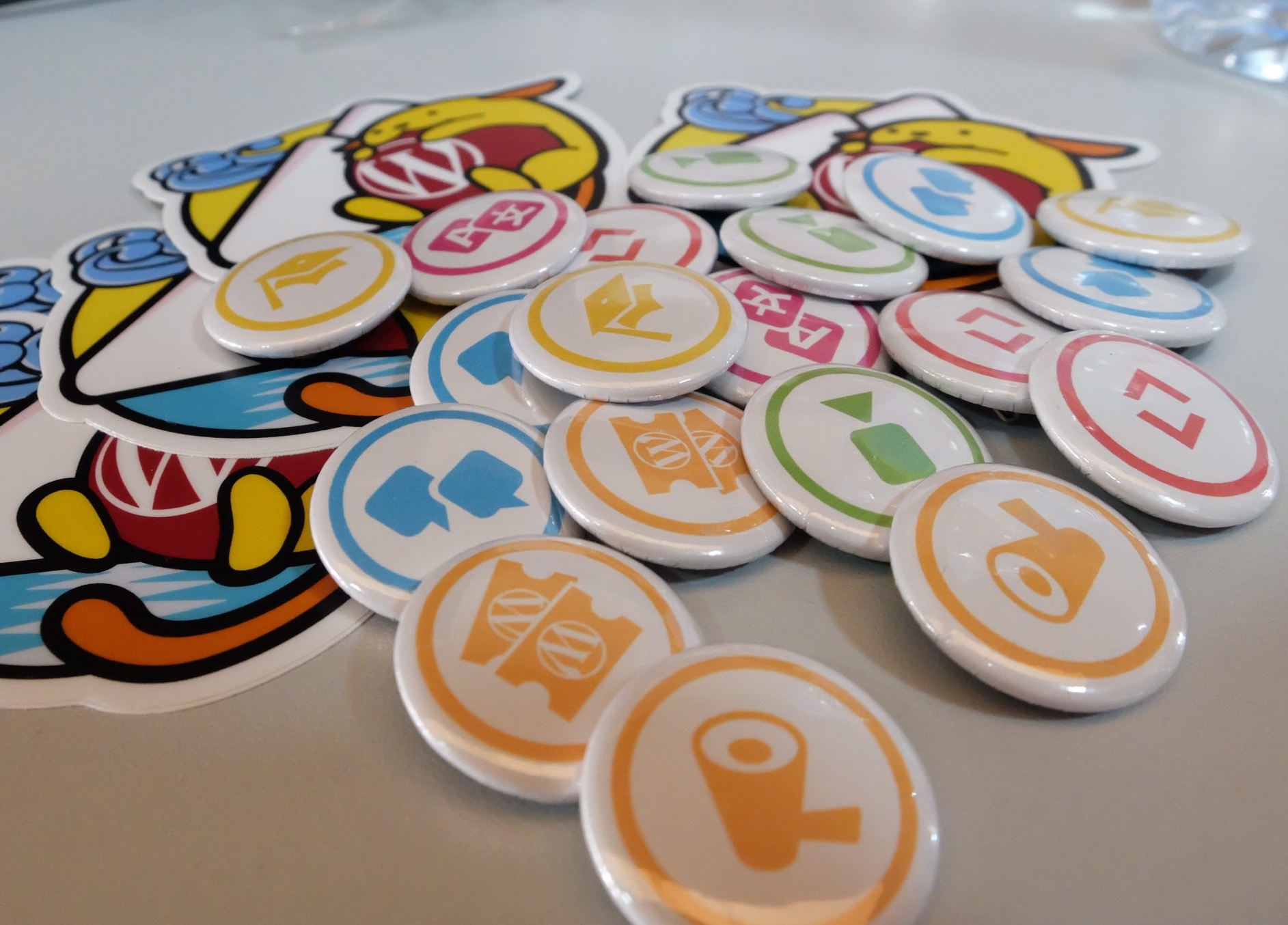 WordPress.org contributor pins and Wapuu stickers on a table. Photo by Pablo Moratinos.