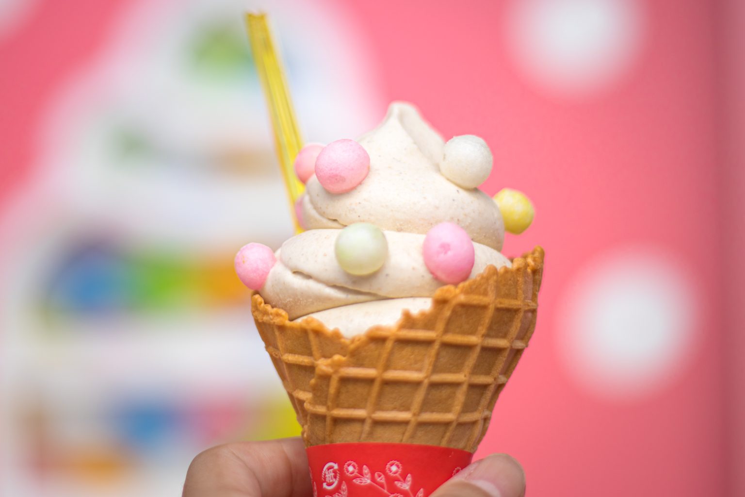 Hand with ice cream cone on a colorful blurred background. The photo is taken at Harajuku Takeshita Street, Japan, by Sysbird.